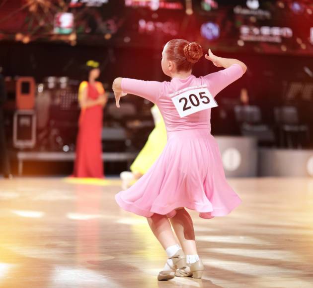 Behind the dancer - a girl dancer-athlete in a pale pink dress against the background of the stage.